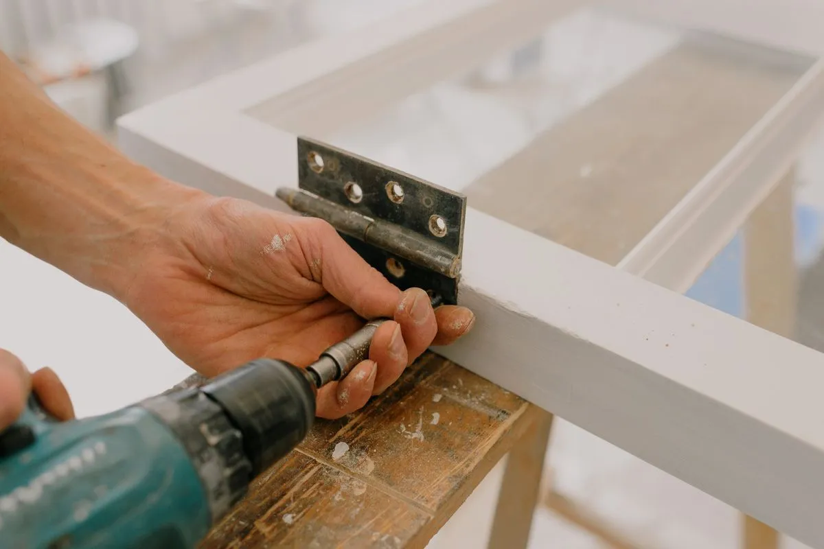 Handyman fitting a hinge to a door frame with a drill