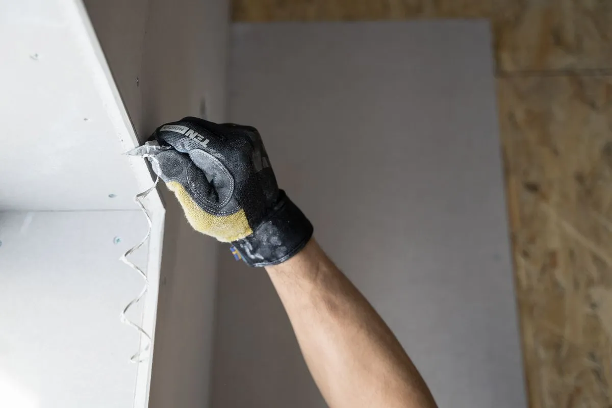 Handyman smoothing a drywall corner with a taping knife