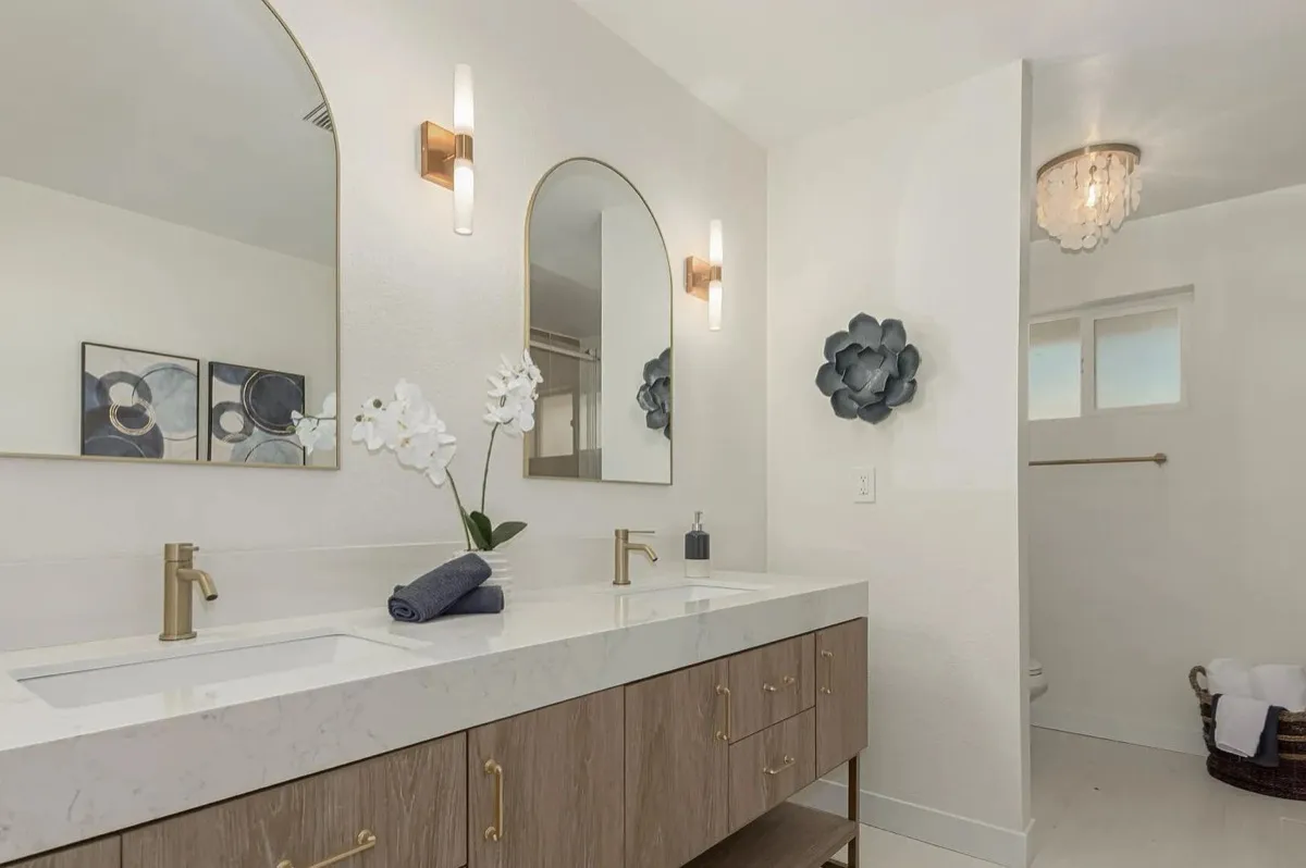 Remodeled bathroom with a double vanity, arched mirrors and gold fixtures